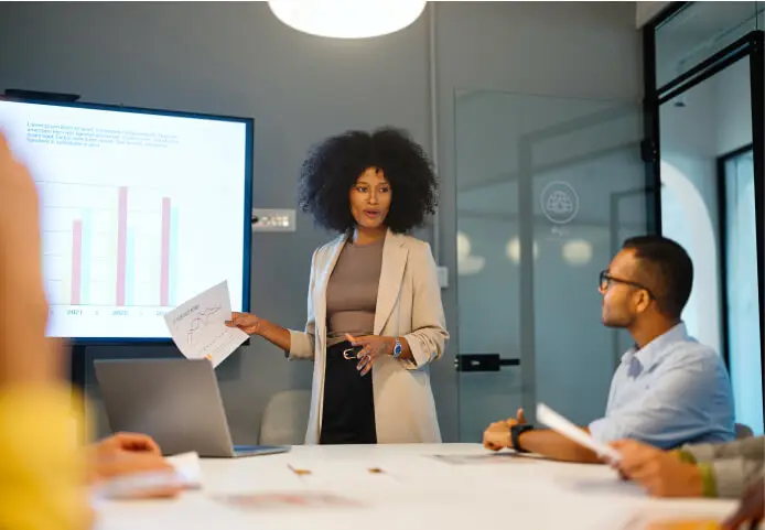 A professional presents data charts to a team in a modern conference room with a screen display.