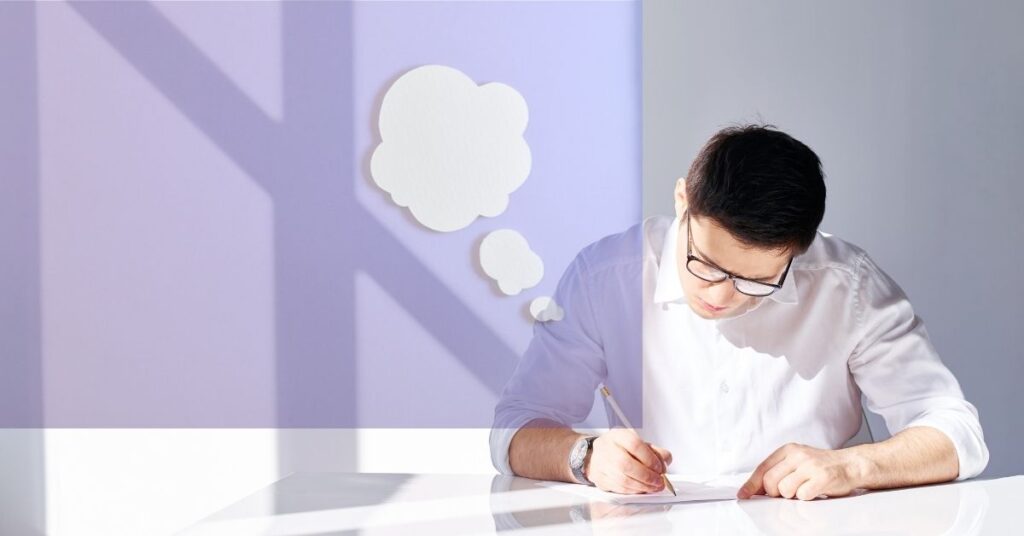 Person writing at desk with thought bubbles, representing how to write a business plan
